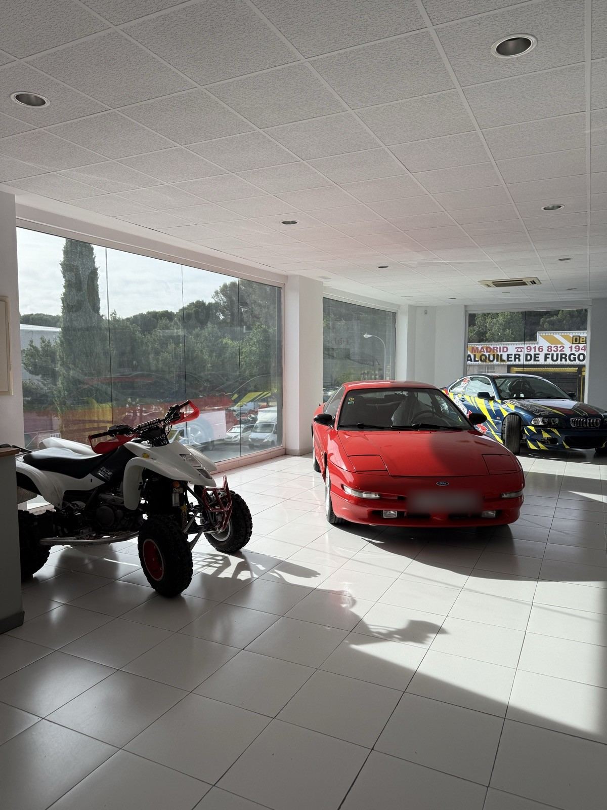Exposición con un coche rojo, un quad y un coche de competición